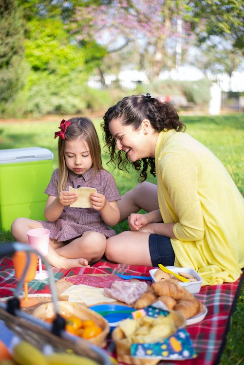A mother and daughter having a picnic with plates of food in front of them