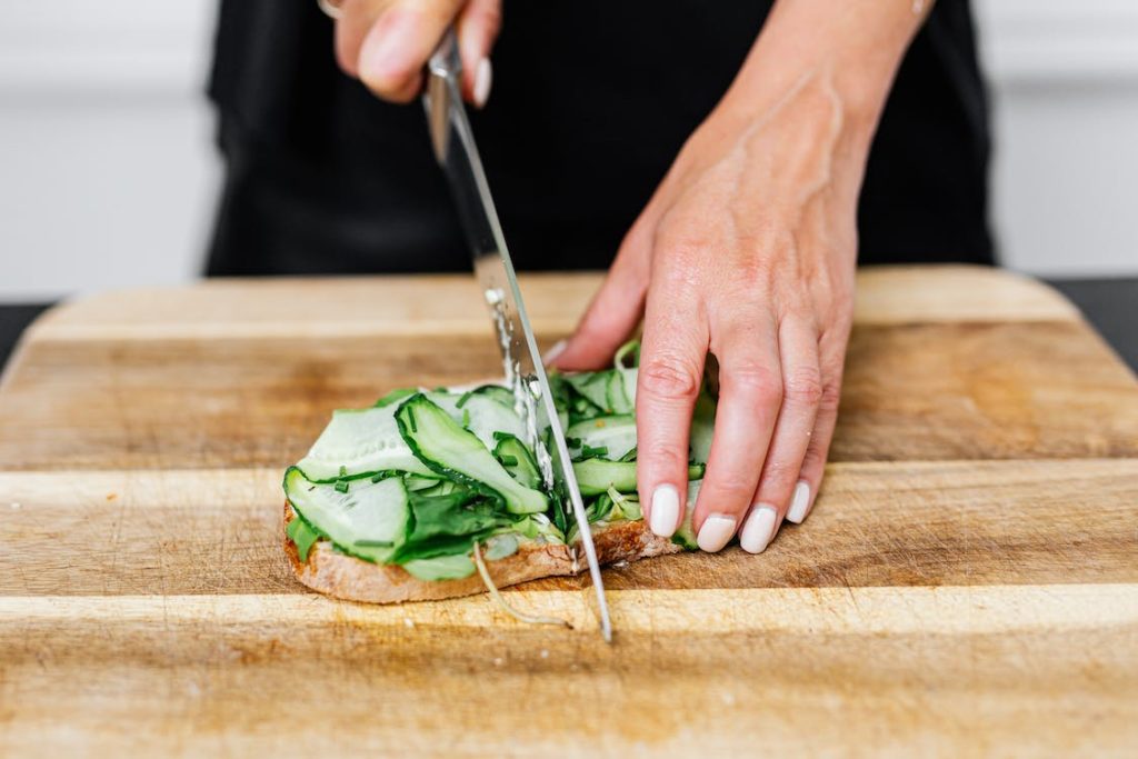 A person Slicing a Sandwich with Cucumber Slices
