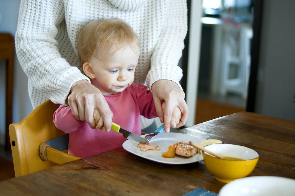 A woman helping a child cut some food in a plate