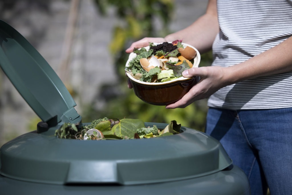 A woman putting food waste into composting tumbler