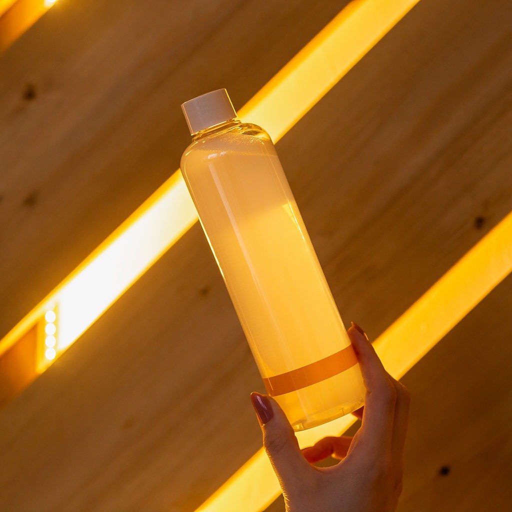 A woman's hand holds an orange transparent container that contains shampoo or lotion.