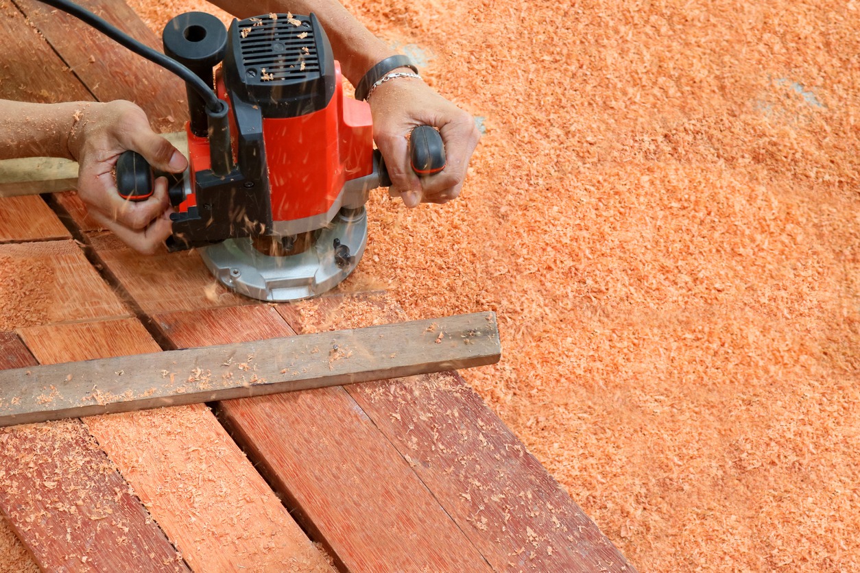 A worker using electric routering to cut down stripes on the wood and sawdust