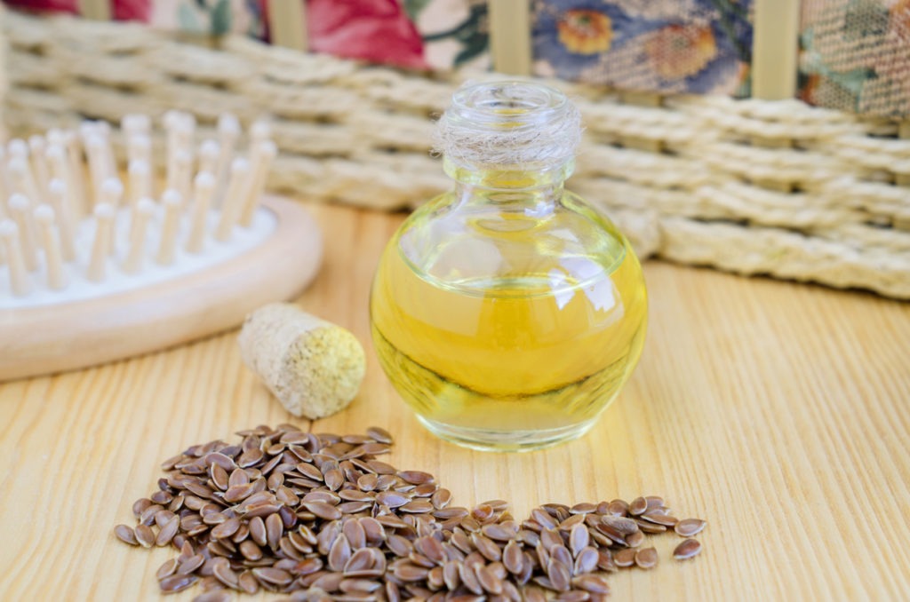 An opened small bottle of flaxseed oil, flaxseeds and a hair brush in a table.