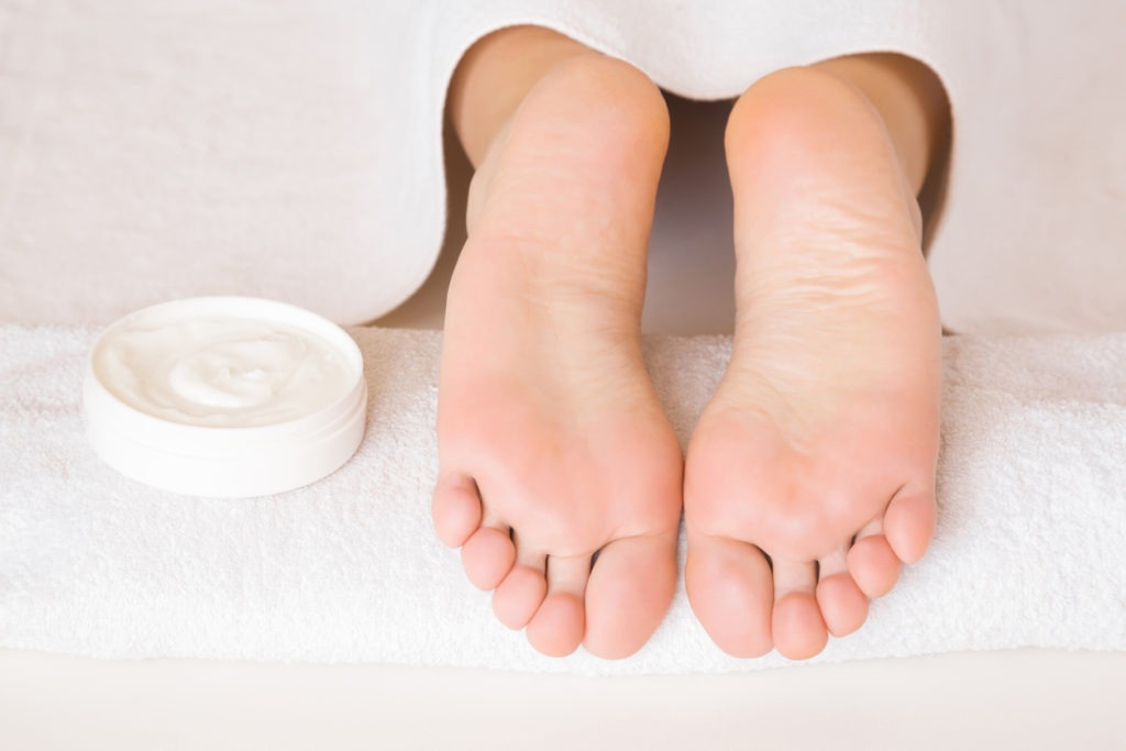 Beautiful woman's foot on a white towel with a cream jar. 