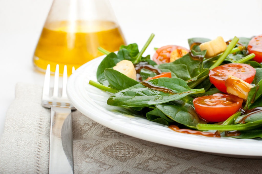 Beautifully plated spinach salad with olive oil and balsamic vinegar in a glass bottle on the background. 
