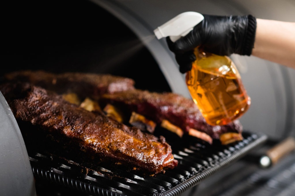 Chef sprinkling grilled meat in a cropped image. 