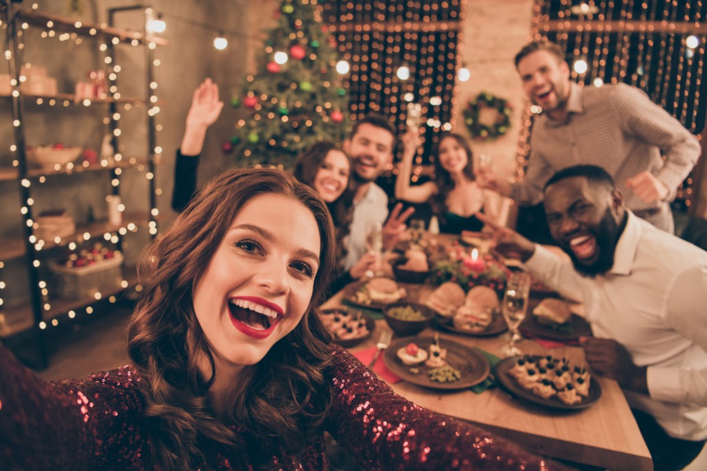 Close-up-photo-of-cheerful-fellows-in-formal-wear-sit-around-table-enjoy-christmas-party-making-selfie-in-house-full-of-noel-decoration