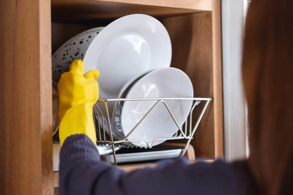 Closeup image of a housewife wearing protective glove, washing and putting dishes in the dish rack