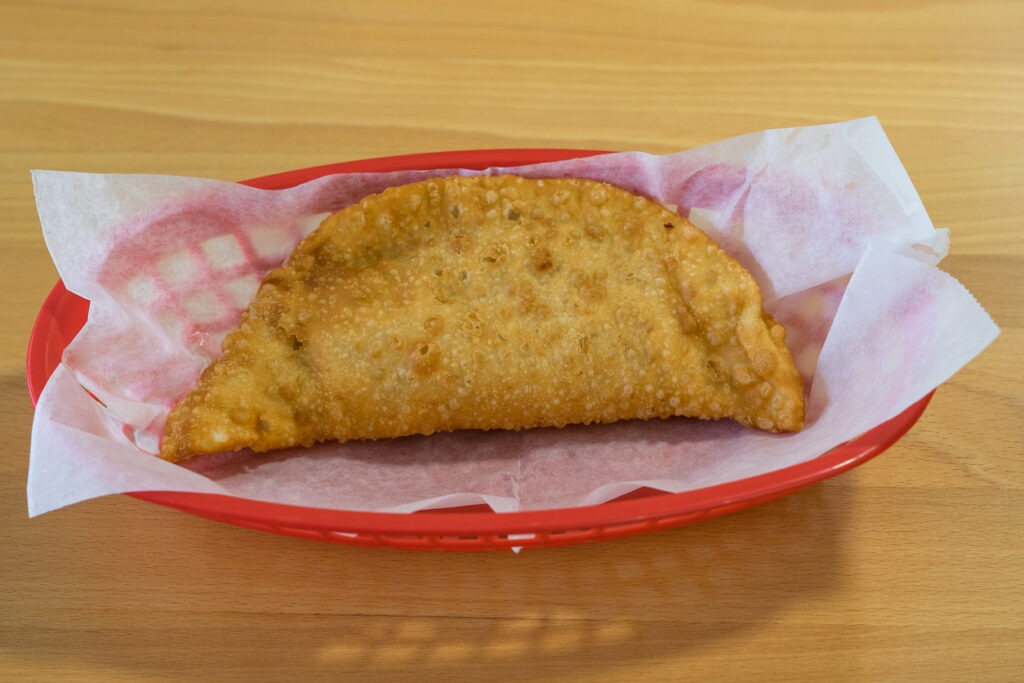 Freshly fried empanadas in a plastic basket with parchment paper