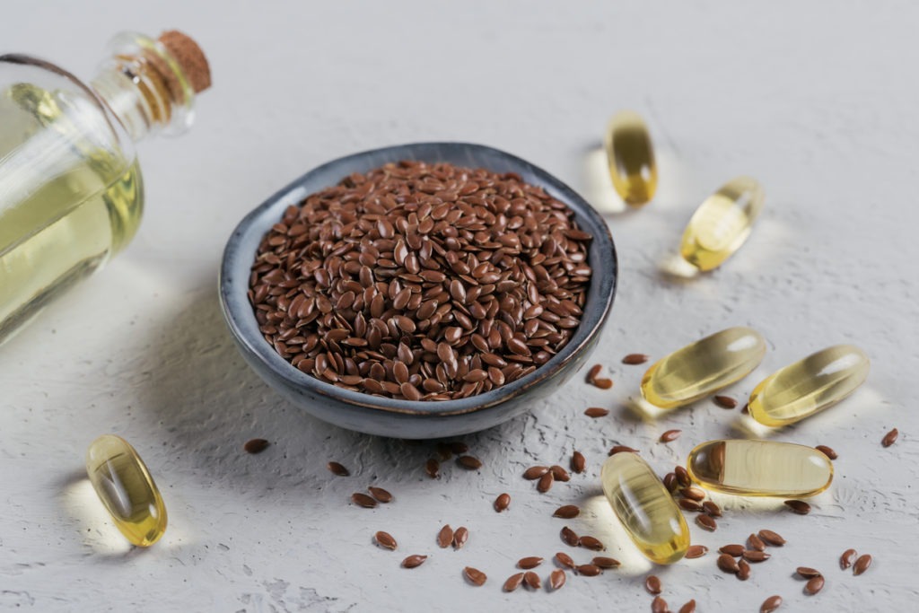 Gelatin capsules with oil and browned flax or linseed in a small bowl.