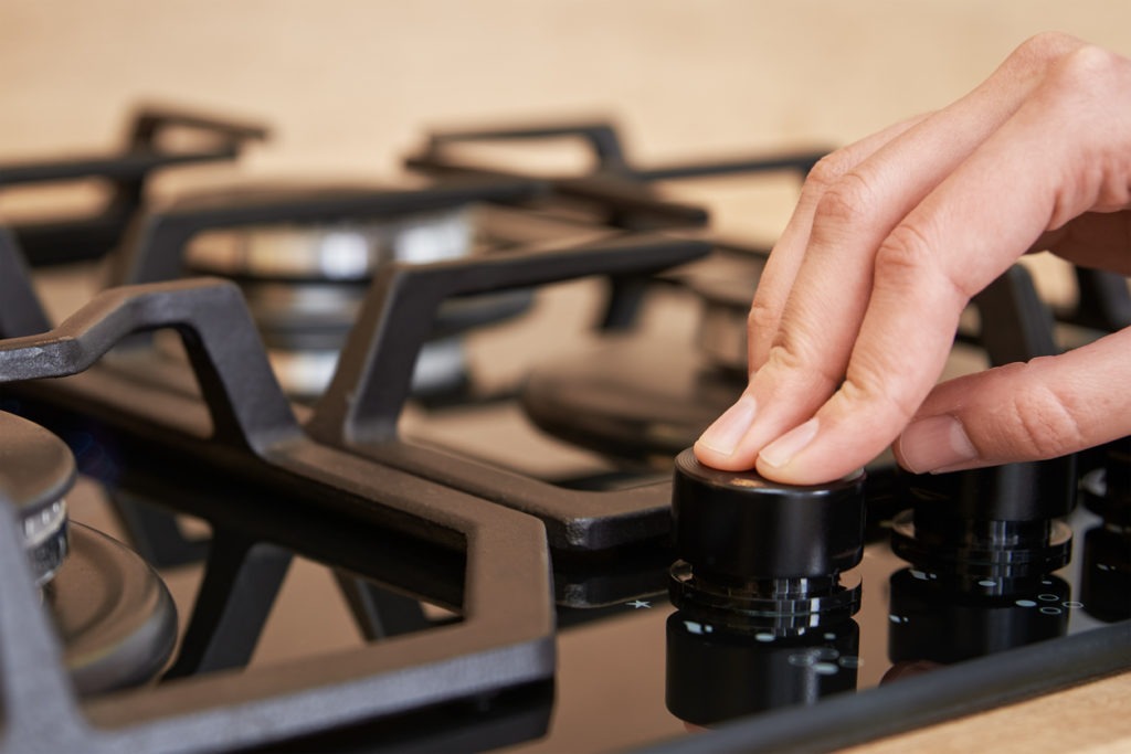 Hand adjusting the temperature knob of gas stove to lower heat
