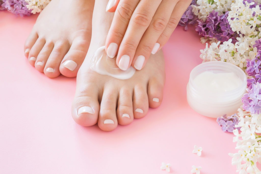 Hands of a young woman applying a natural cream moisturizer on perfectly groomed feet. 