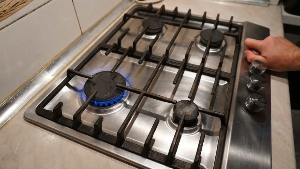 Hands turning the control knobs of a gas stove to ignite the heat