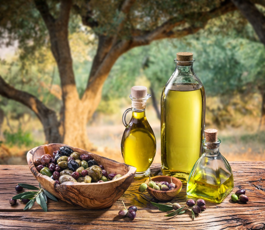 In the background, an olive grove at dusk with olives and a bottle of olive oil. 