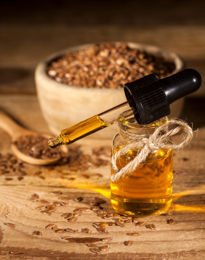 Linseed oil, a bowl, and a spoon with linseeds on a wooden background.