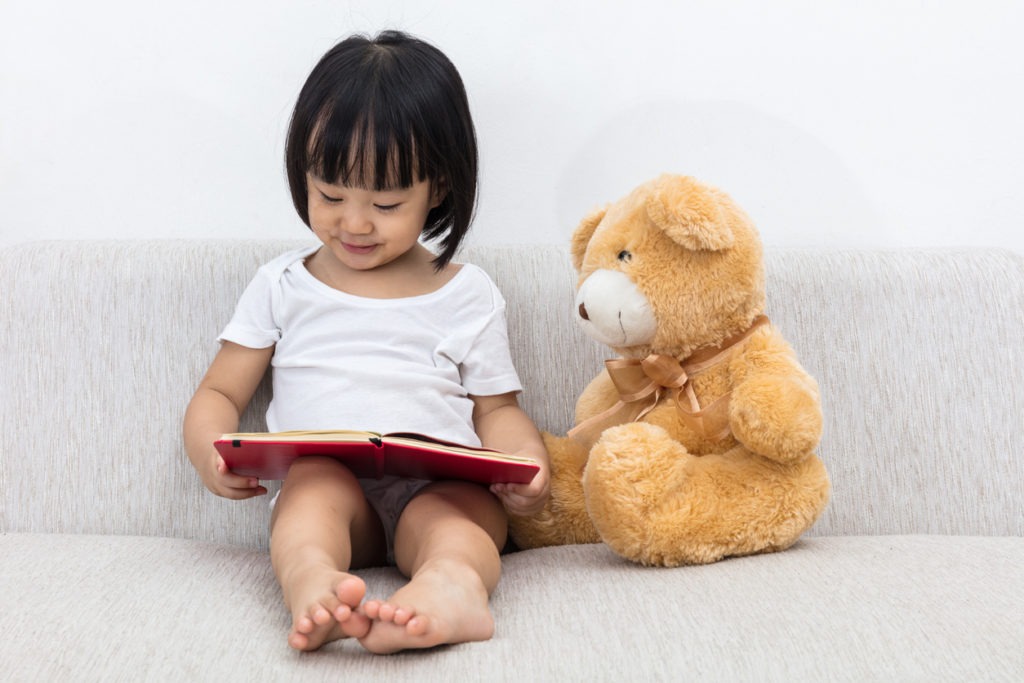Little girl reading book with teddy bear