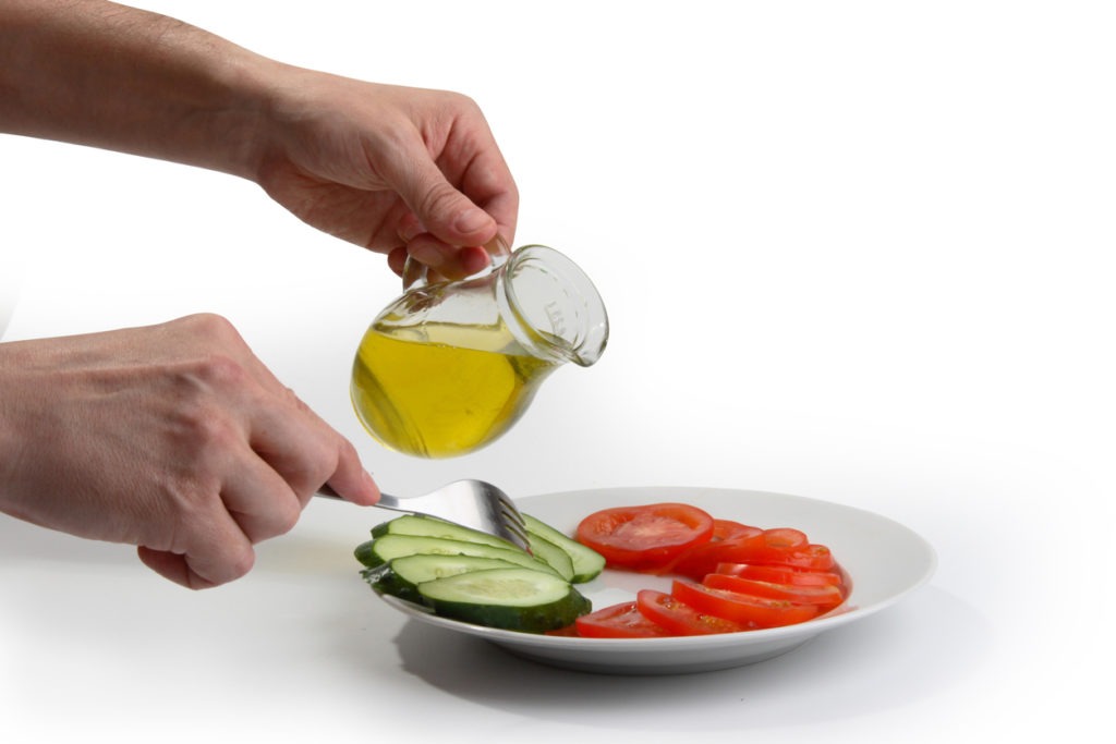 Man pouring olive oil on cucumbers and tomatoes as they are being chopped 