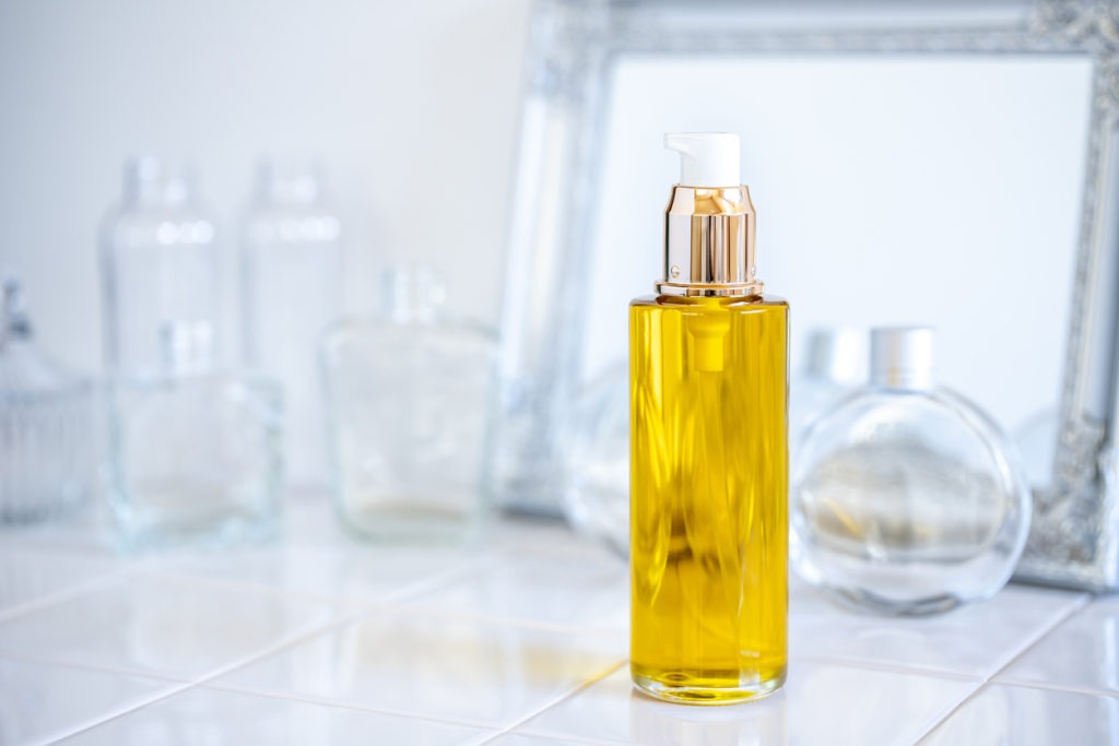 Moisturizing oil in a bottle on top of the table with empty bottles on the background. 