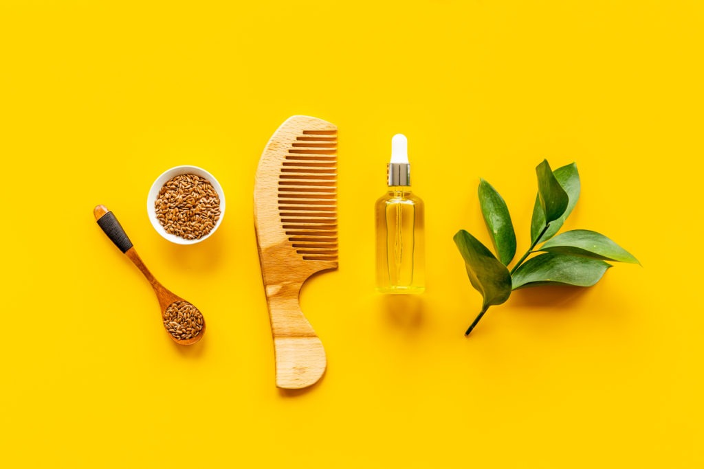 Oil for hair treatment with seeds and a wooden comb.
