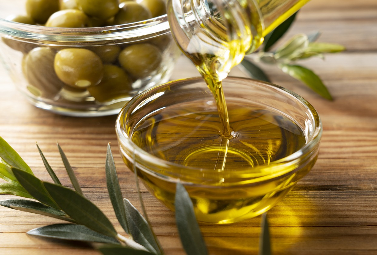 Olive oil is poured into a glass bowl from a glass bottle on a wooden table.