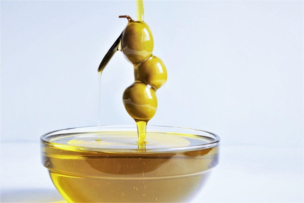 Olive oil pouring with three olives not touching the bowl's rim, white background. 