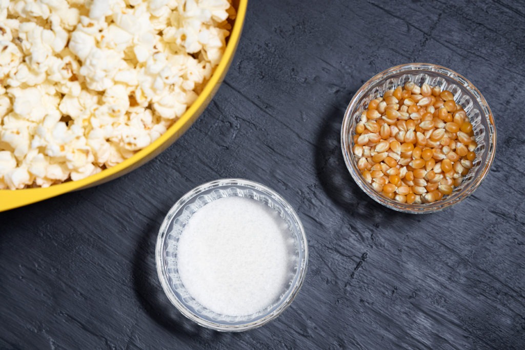Popcorn in a yellow bowl next to corn kernels and salt