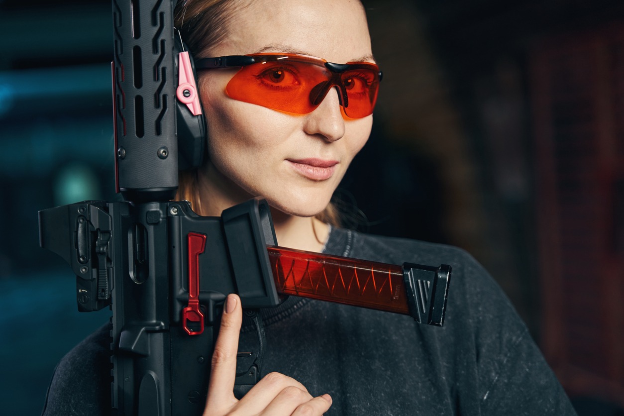 Portrait of young shooter in safety goggles demonstrating her firearm for the camera