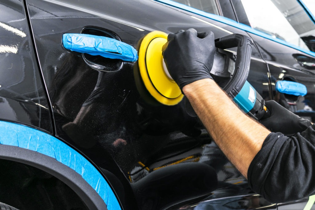 Professional wearing gloves buffing a car using a buffer. 