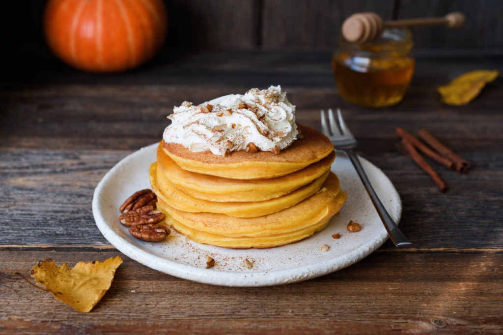 Pumpkin pancakes with whipped cream and cinnamon on an old wooden table. Autumn comfort food, breakfast food
