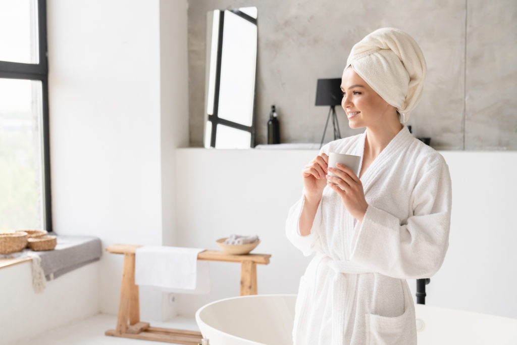 Relaxed-serene-young-woman-girl-in-bath-spa-towel-and-bathrobe-drinking-water-hot-beverage-after-shower-bath-at-home