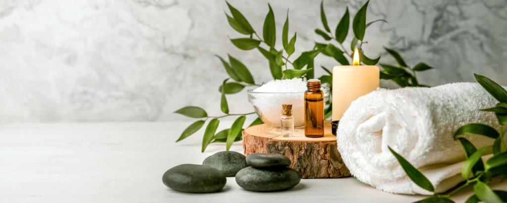 Spa operations' beauty supplies are displayed on a white wooden table with massage stones, essential oils, and sea salt. 