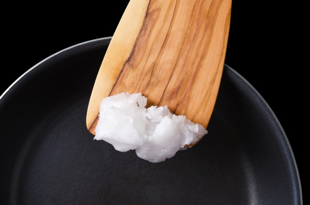 Spreading coconut oil on a pan with a wooden spatula.