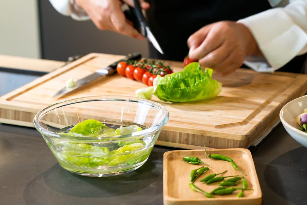 Vegetable green oak in a water glass bowl with chef's hand preparing material behind