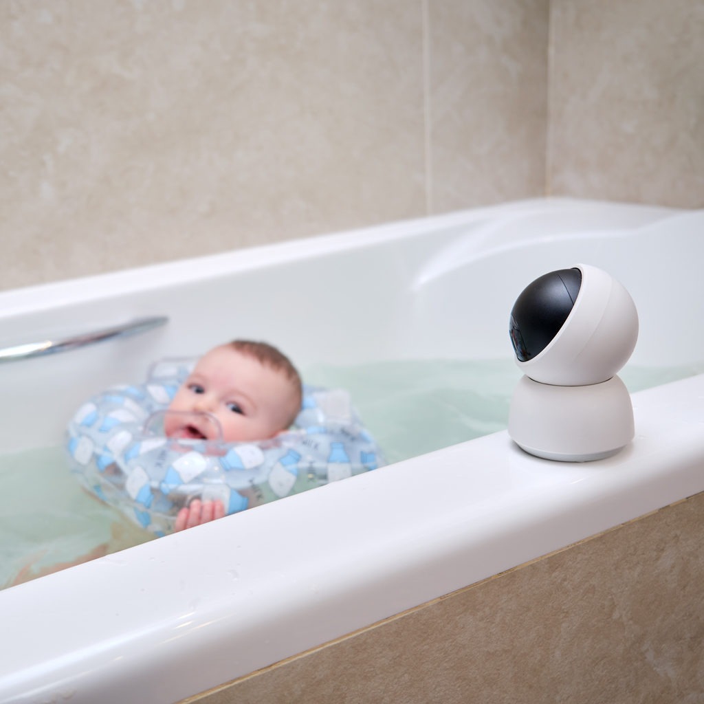 Infante baby bathes in a home bathroom under the supervision of an online video camera
