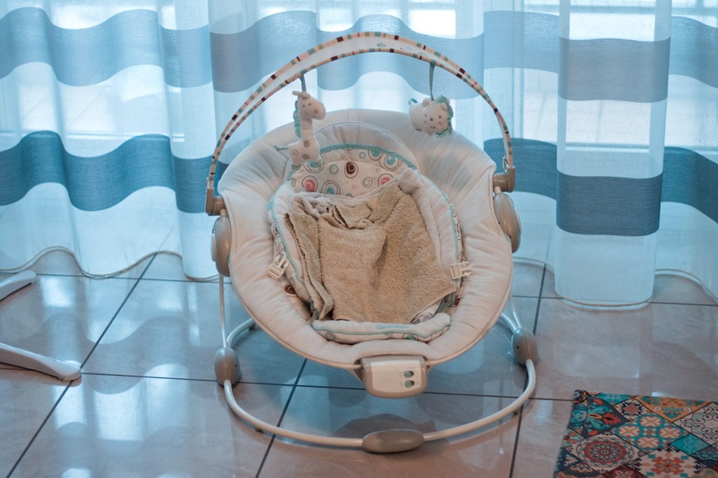 A baby bouncer with toys and towels on the ground in front of a striped curtain in the living room (Marche, Italy, Europe)
