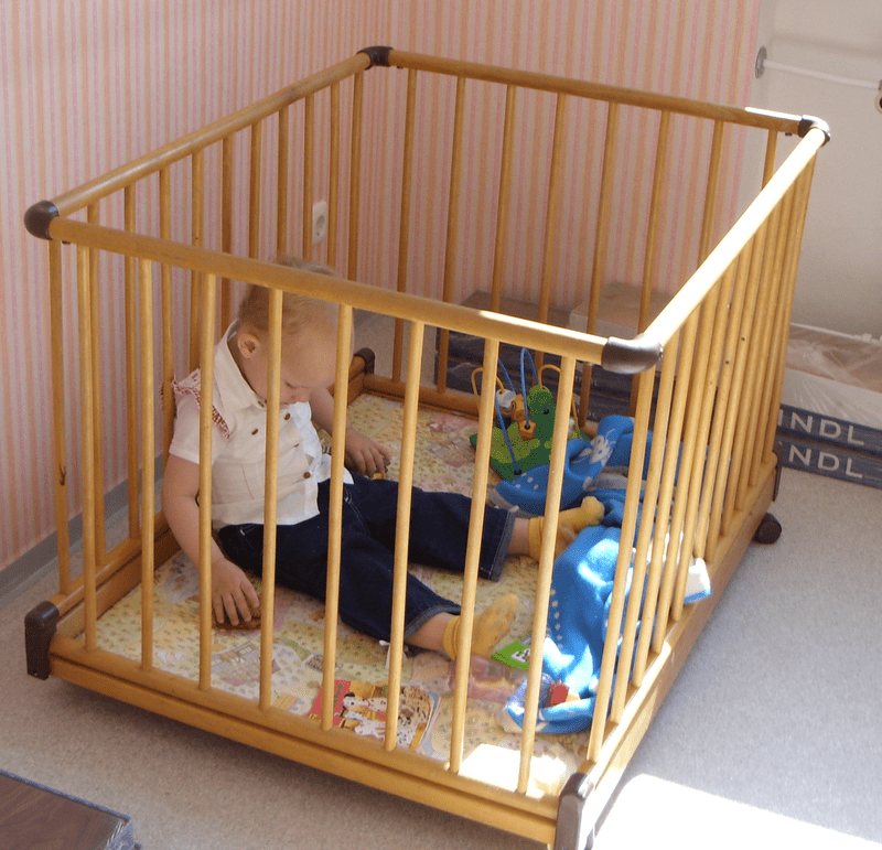 A baby boy inside a wooden playpen