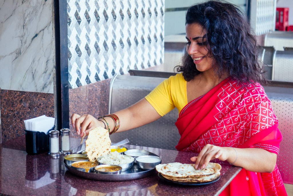 beautiful brunette woman in red sari eating with appetite traditional thali wirh rise,curd,dal in Goa restaurant masala tea