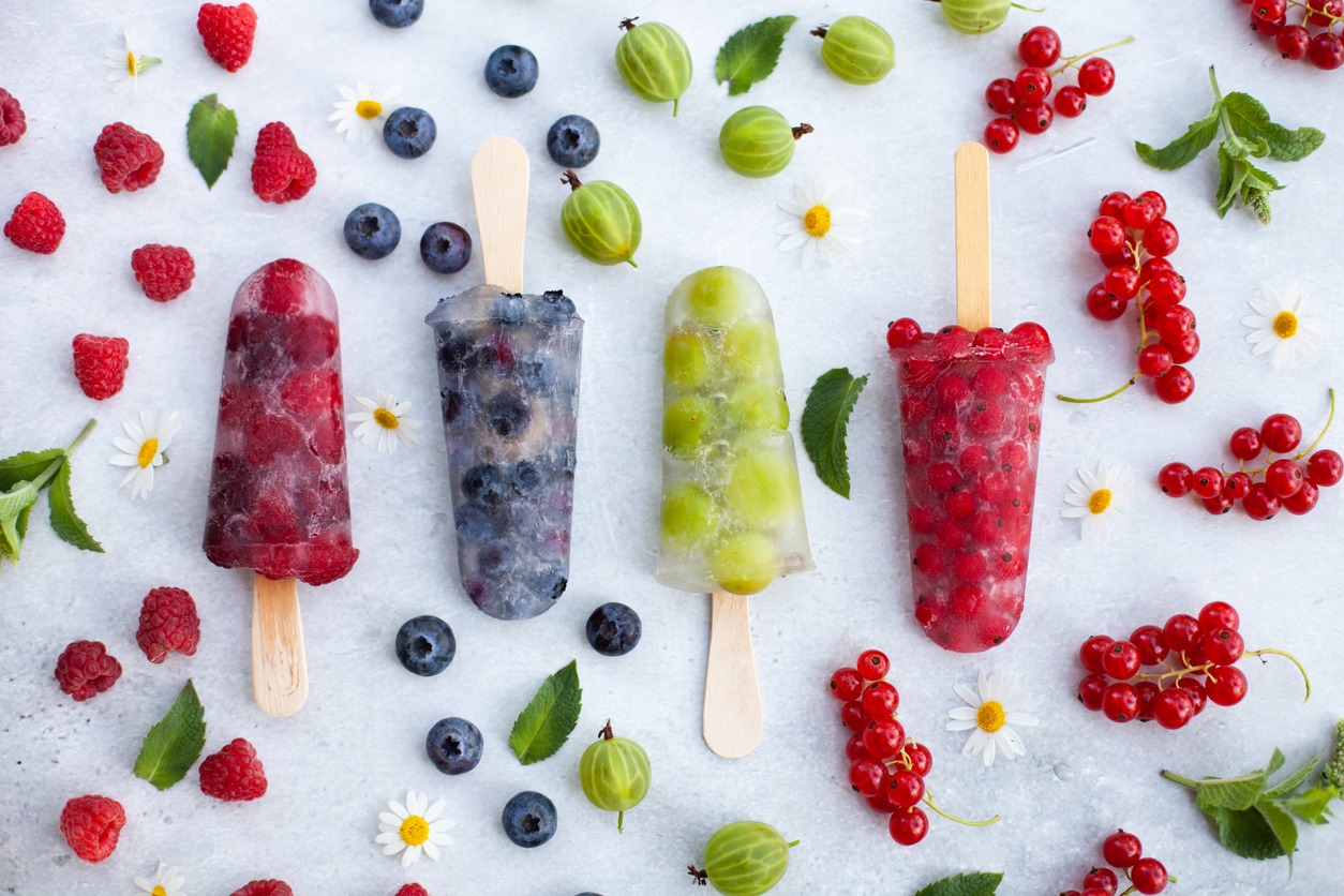 Four frozen ice cream popsicles with raspberries, gooseberries, blueberries and red currants.