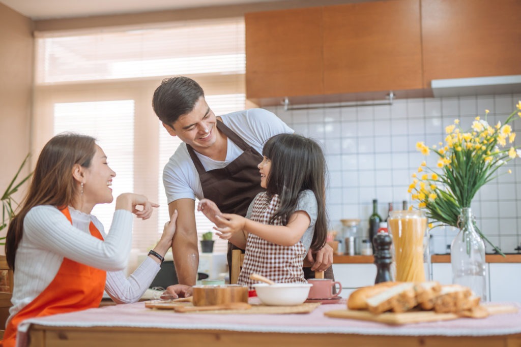 healthy mother, father, and child baking together in a brown-colored kitchen with a messy table of bakeware and bread