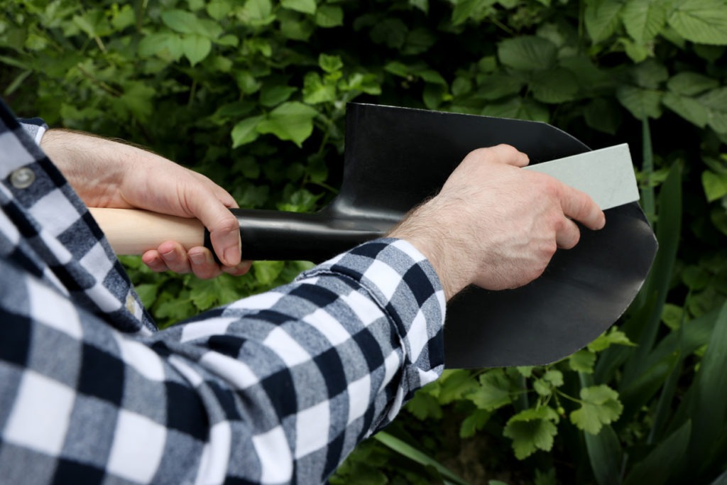 Man sharpening shovel outdoors, closeup. Gardening tools