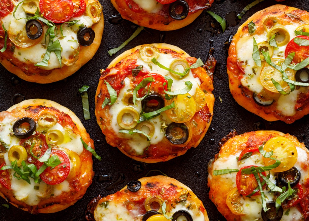 Mini pizzas with the addition of cherry tomatoes, olives, mozzarella cheese and fresh basil on a black background