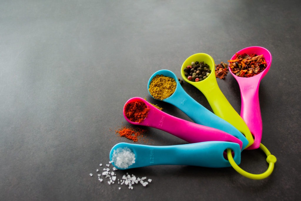 Multicolored measuring spoons with spices: chili flakes, a mix of pepper peas, curry, paprika and coarse sea salt. Black background, copy space