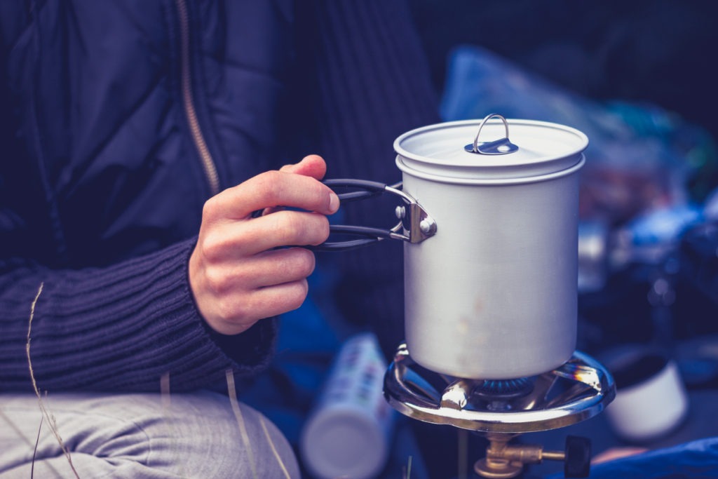 Close up on a woman's hand as she is boiling water in a pot on a portable camping stove