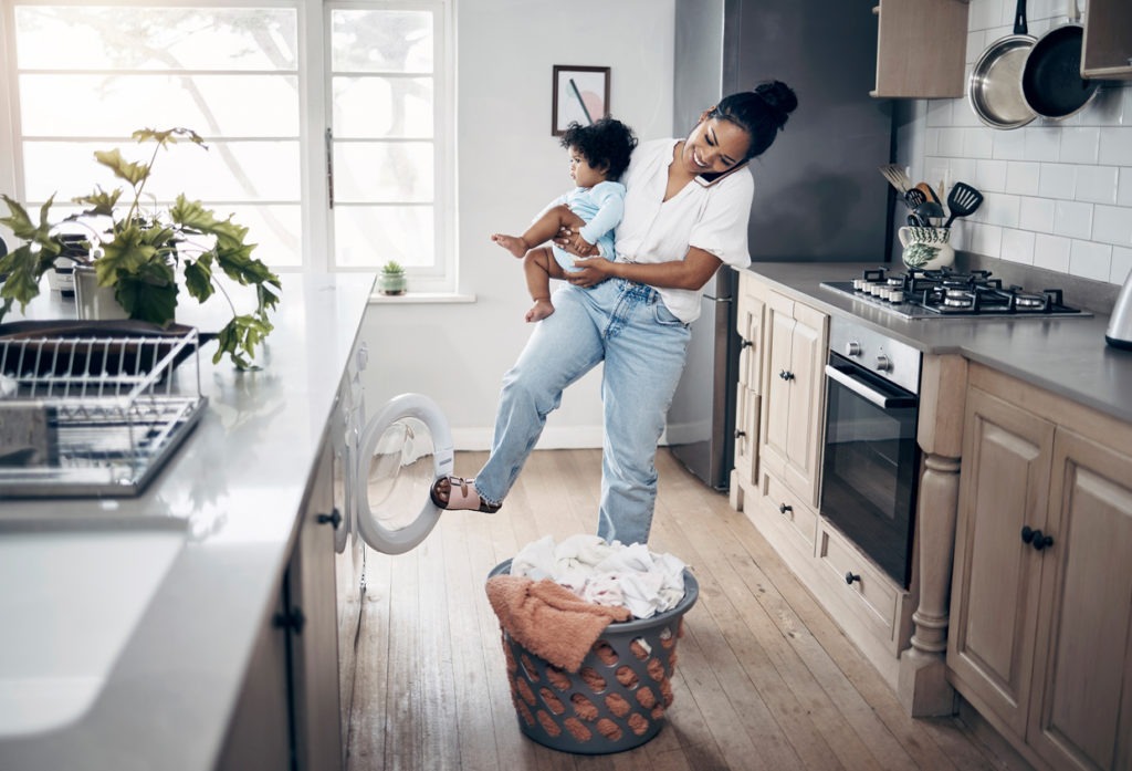 young mother using a cellphone while completing housework