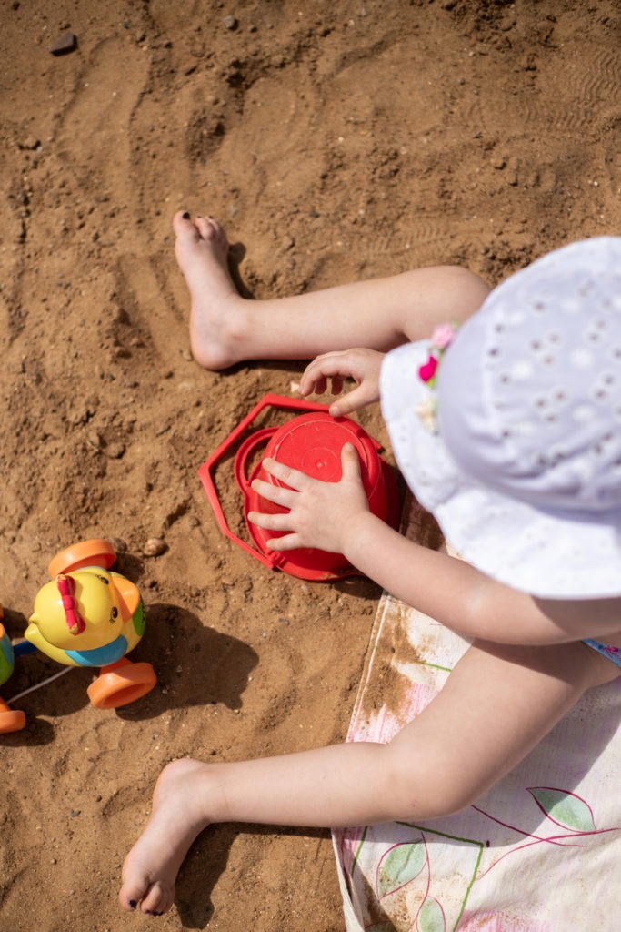 A child in a white sun hat sitting on the beach and playing with sand