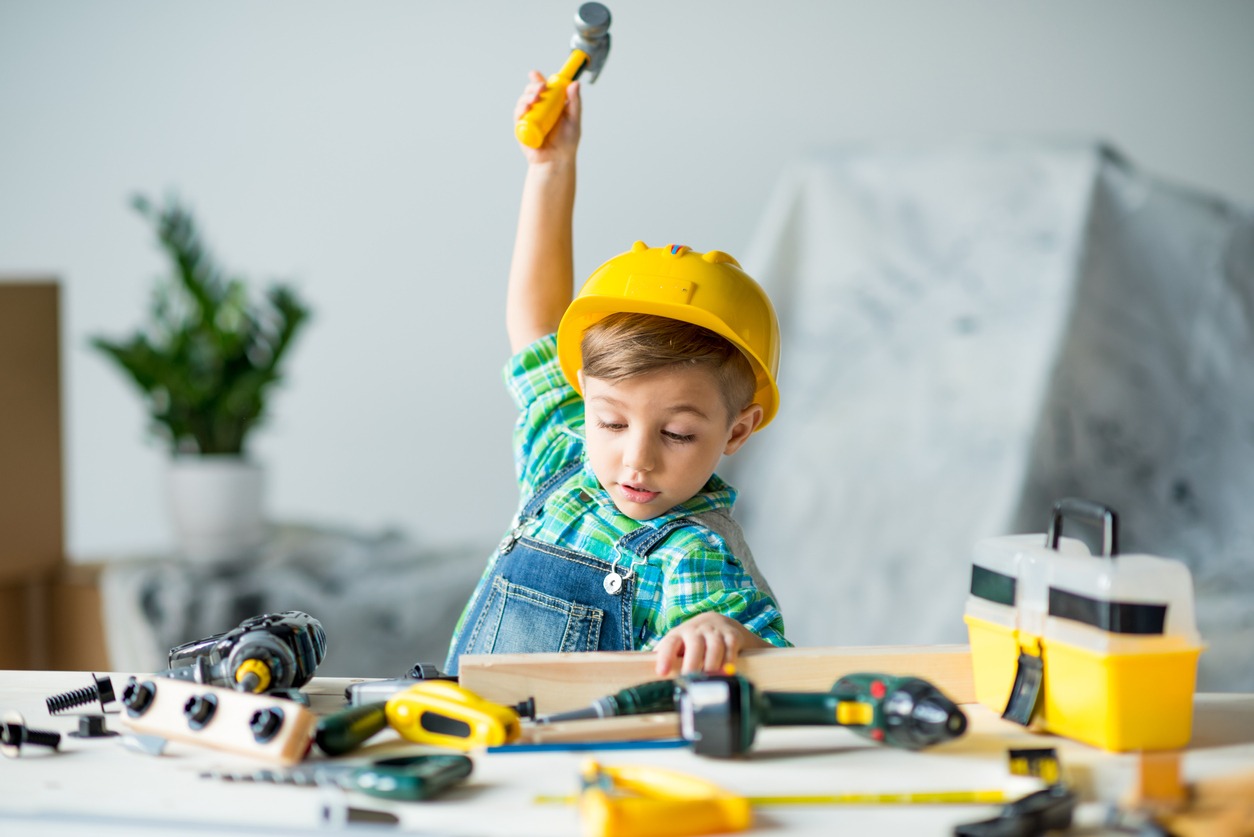 A little boy wearing a hard hat and holding a hammer, acting like a carpenter 