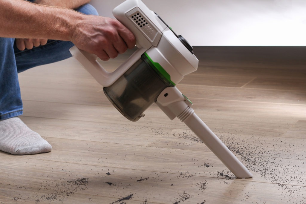 A man using a handheld vacuum duster to clean floor