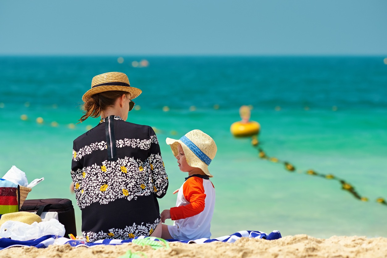 A mother and her toddler wearing sun hats on the beach
