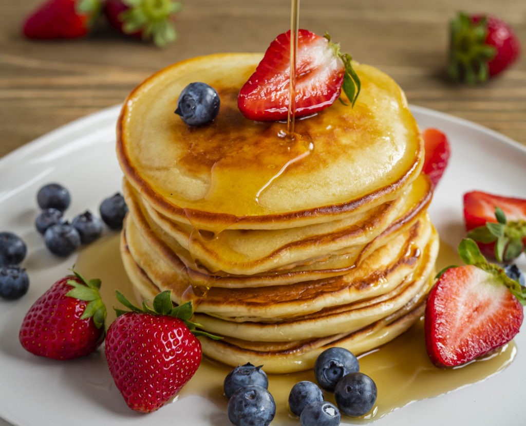 A stack of pancakes with berries and syrup as toppings
