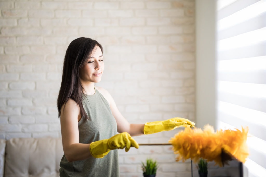 A woman cleaning a television using feather duster